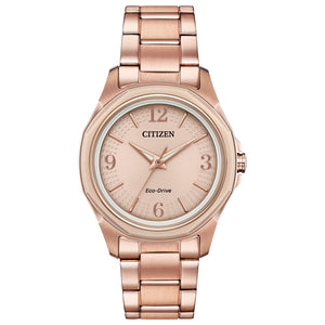 Citizen FE7053-51X Drive watch featuring a pink gold-tone stainless steel case, light pink dial with luminous rose gold-tone dauphine-style hands and index hour markers, Arabic numerals at 3, 6, 9, and 12 o'clock positions, and matching bracelet—front view.
